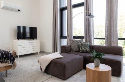 Each Tomorrow Building Apartment Features A Cozy Couch, And Must Have Furnitures To Get You Settled And Easily Moved In. Photo: TV On A Dresser Next To A Wall Of Windows.